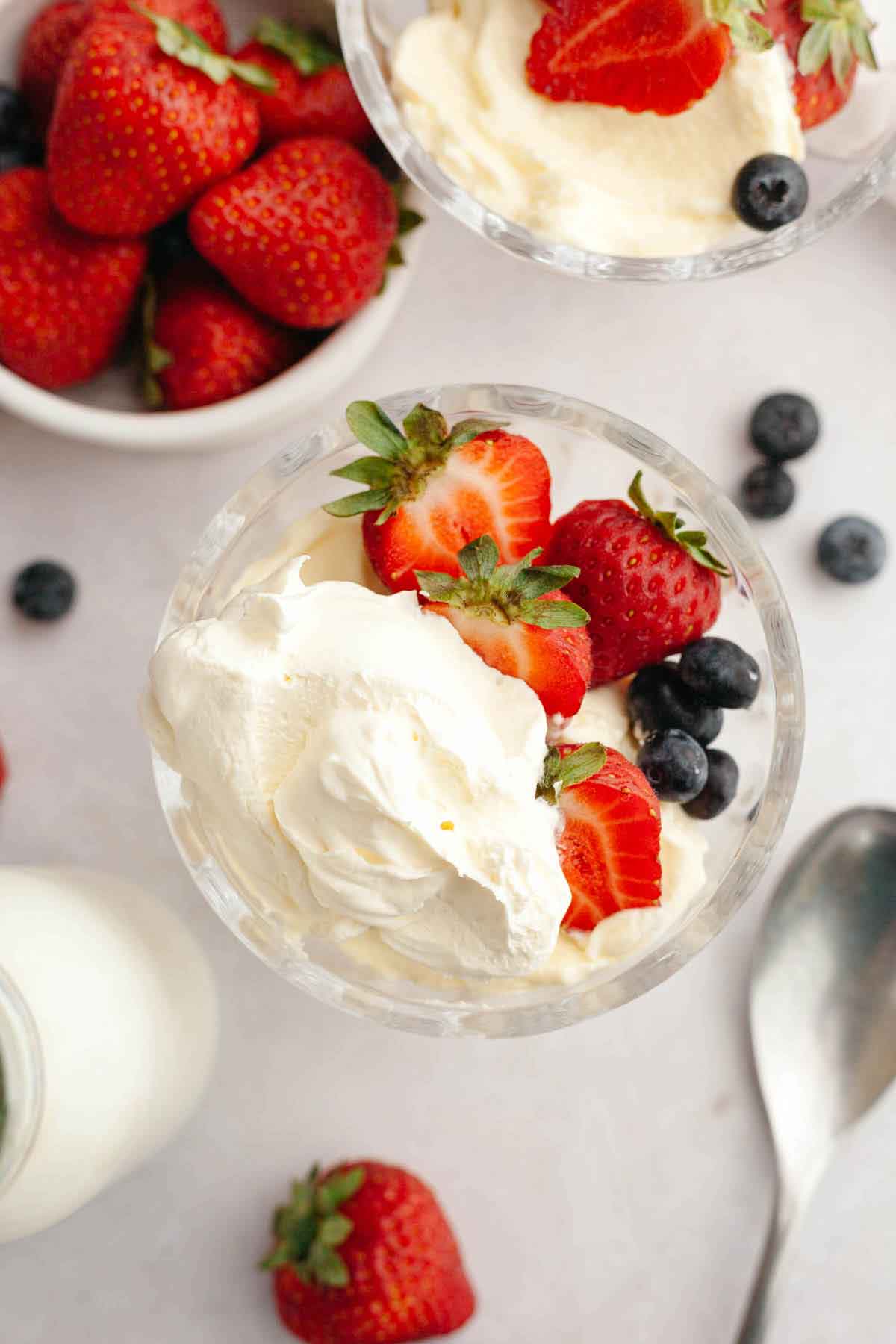 Overhead photo of a glass bowl with strawberries, blueberries, and fresh whipped cream.