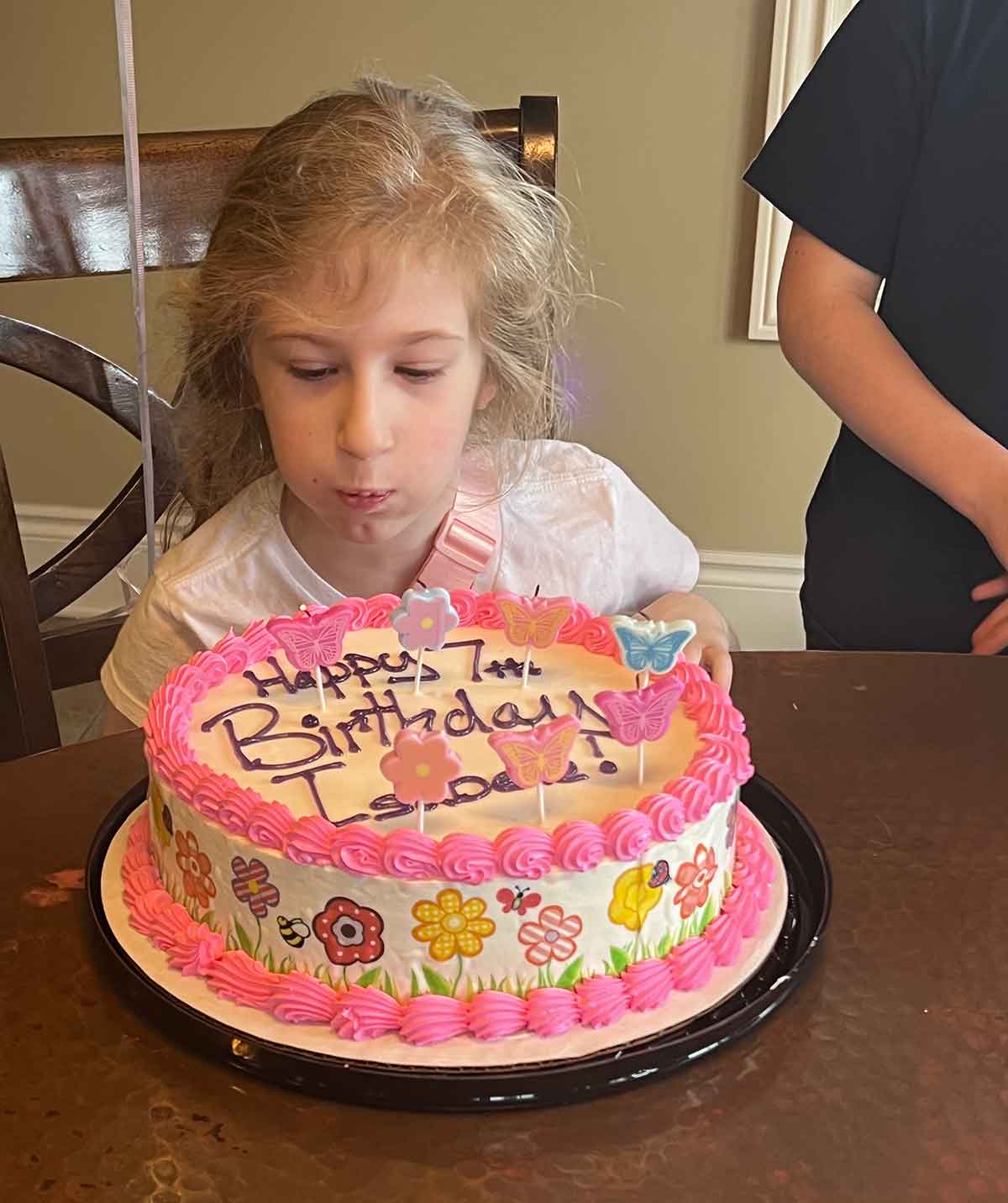Little girl blowing out candles on a birthday cake with flowers and pink icing.