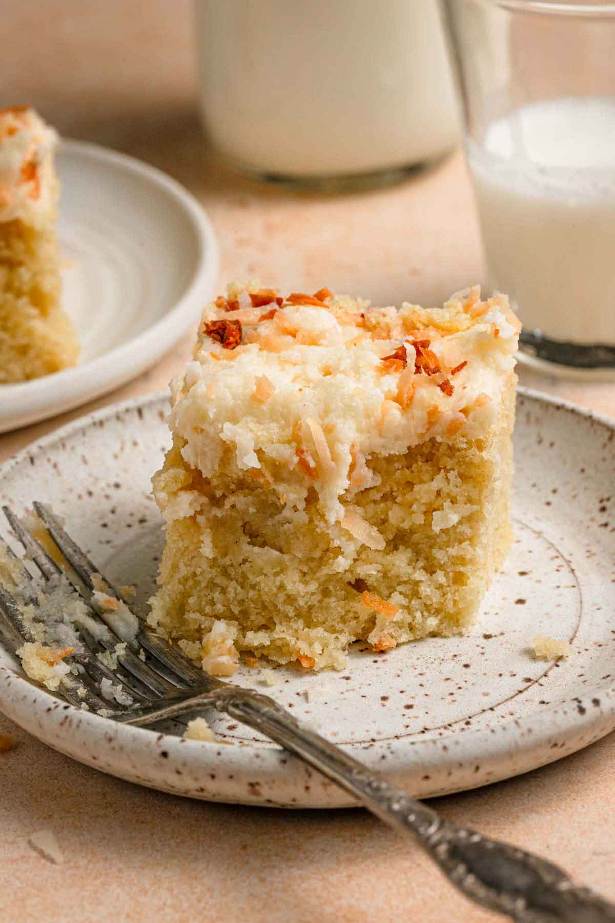 Piece of one-layer coconut cake on a speckled plate with a fork resting on the plate.
