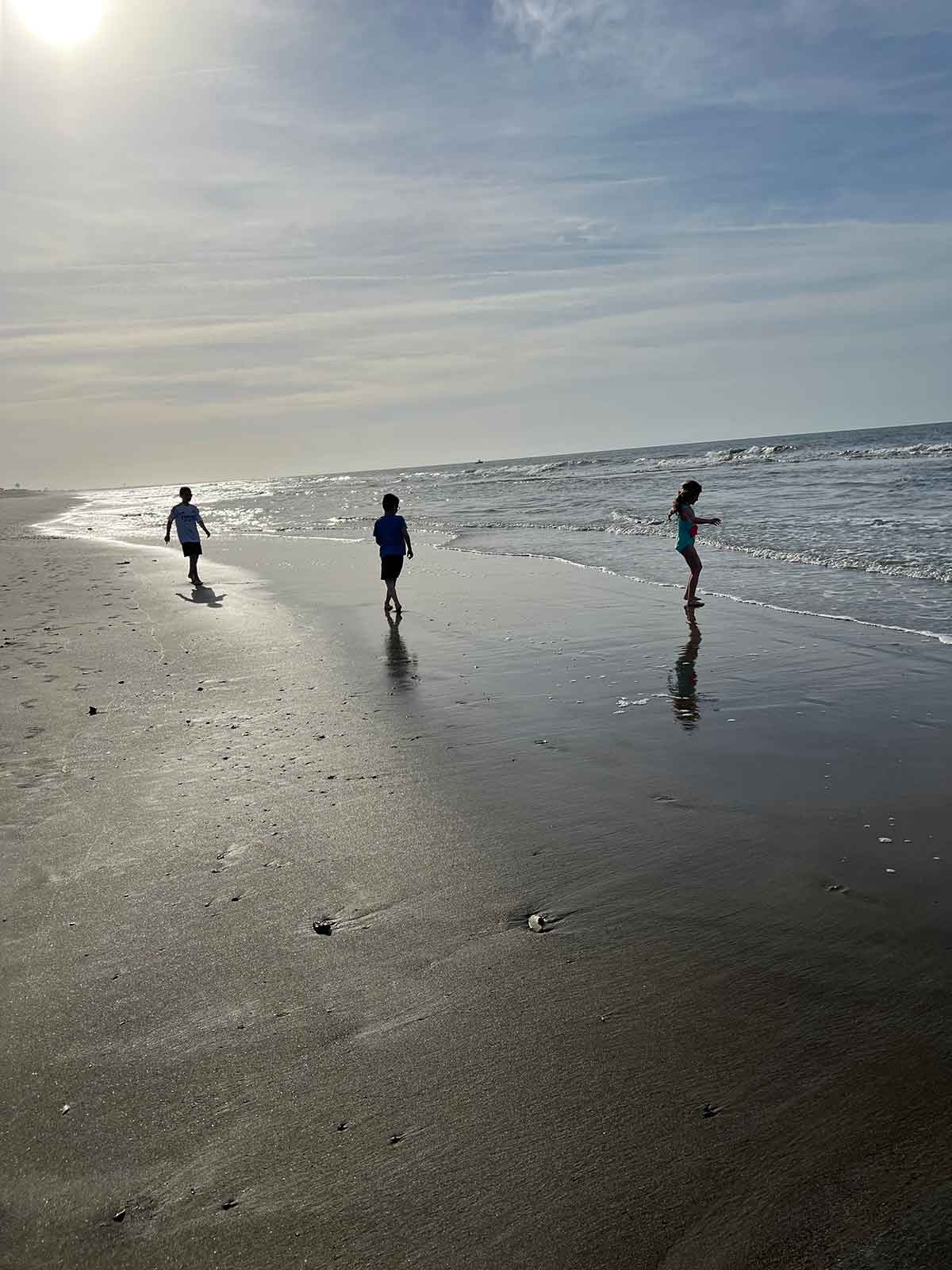 Two boys and a girl playing in the surf of a beach during sunrise.