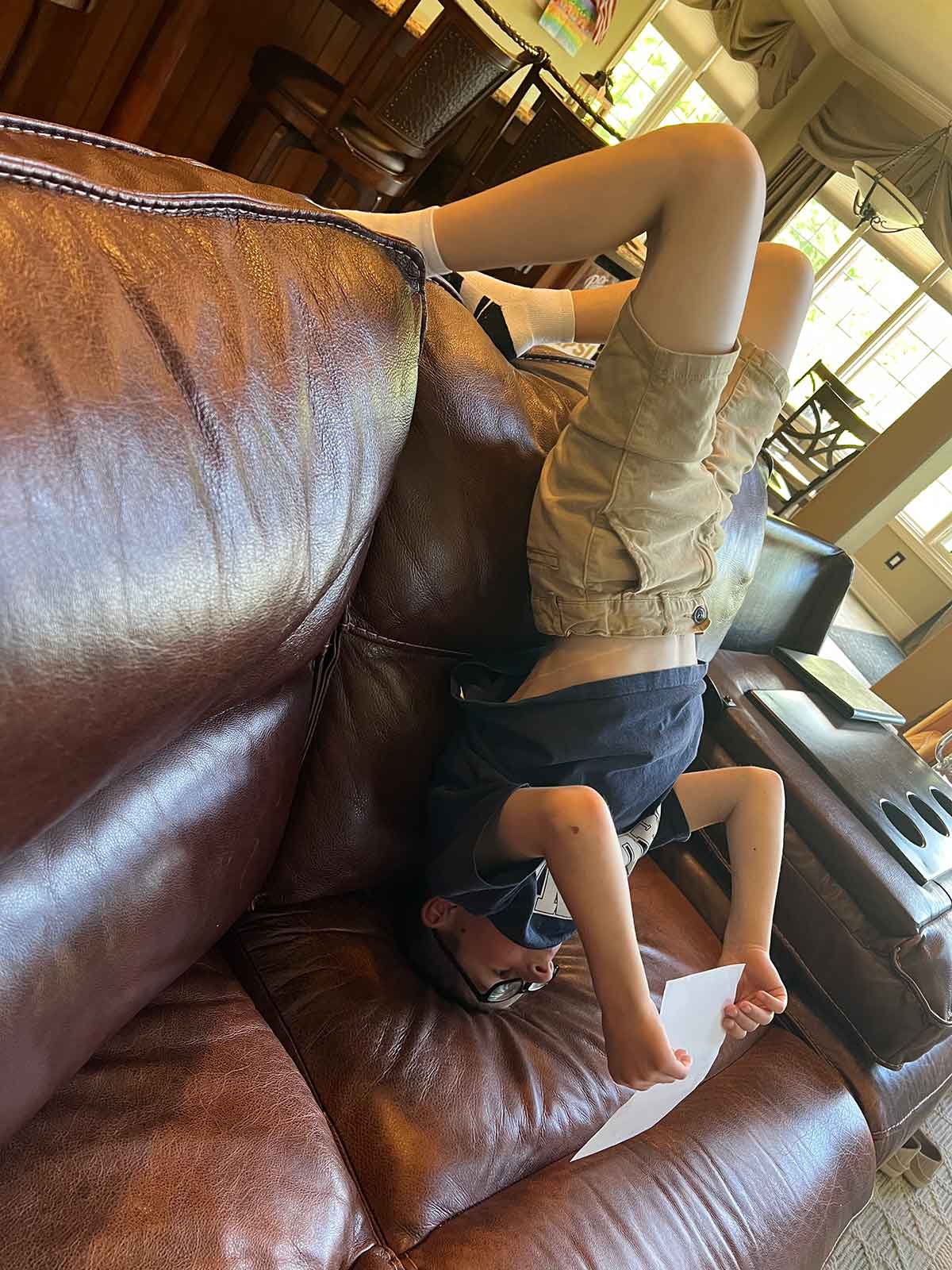 Little boy laying upside down on a couch studying a piece of paper.