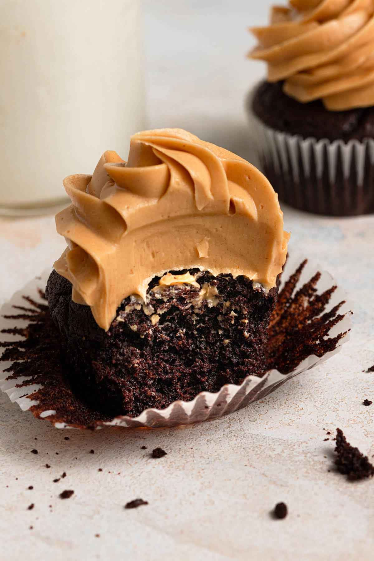 Chocolate cupcake topped with peanut butter frosting, with the wrapped pulled away and the cupcake cut in half.