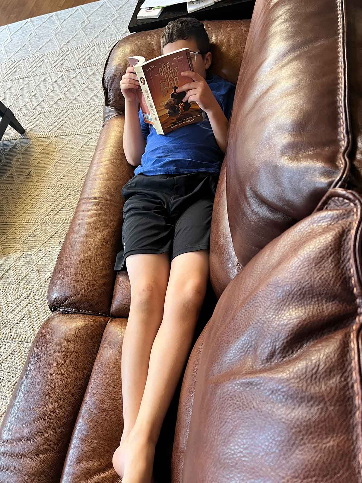 Boy laying on a couch reading a book "The One and Only Bob".