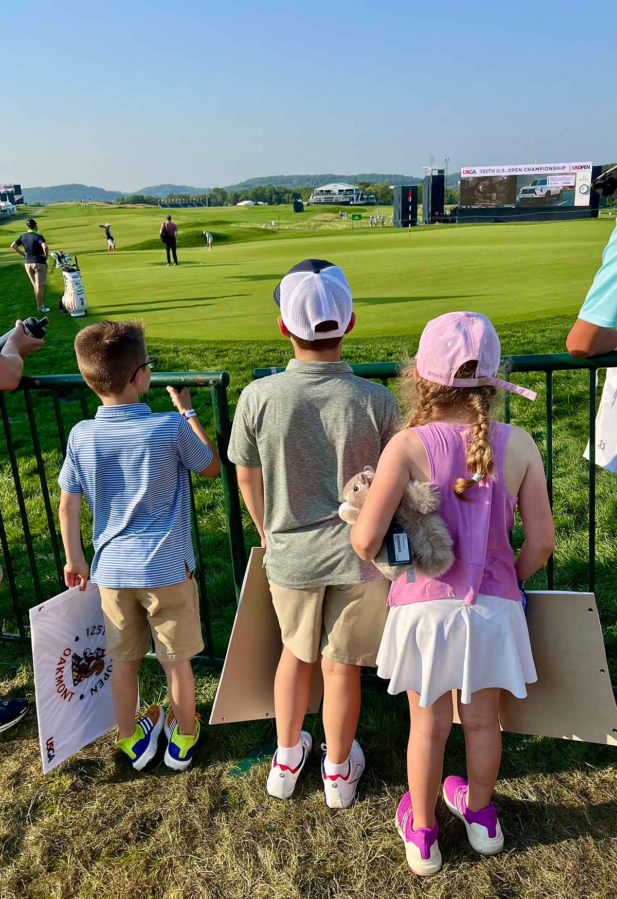 Two boys and a girl standing in front of a putting green, watching a golfer at the U.S. Open.
