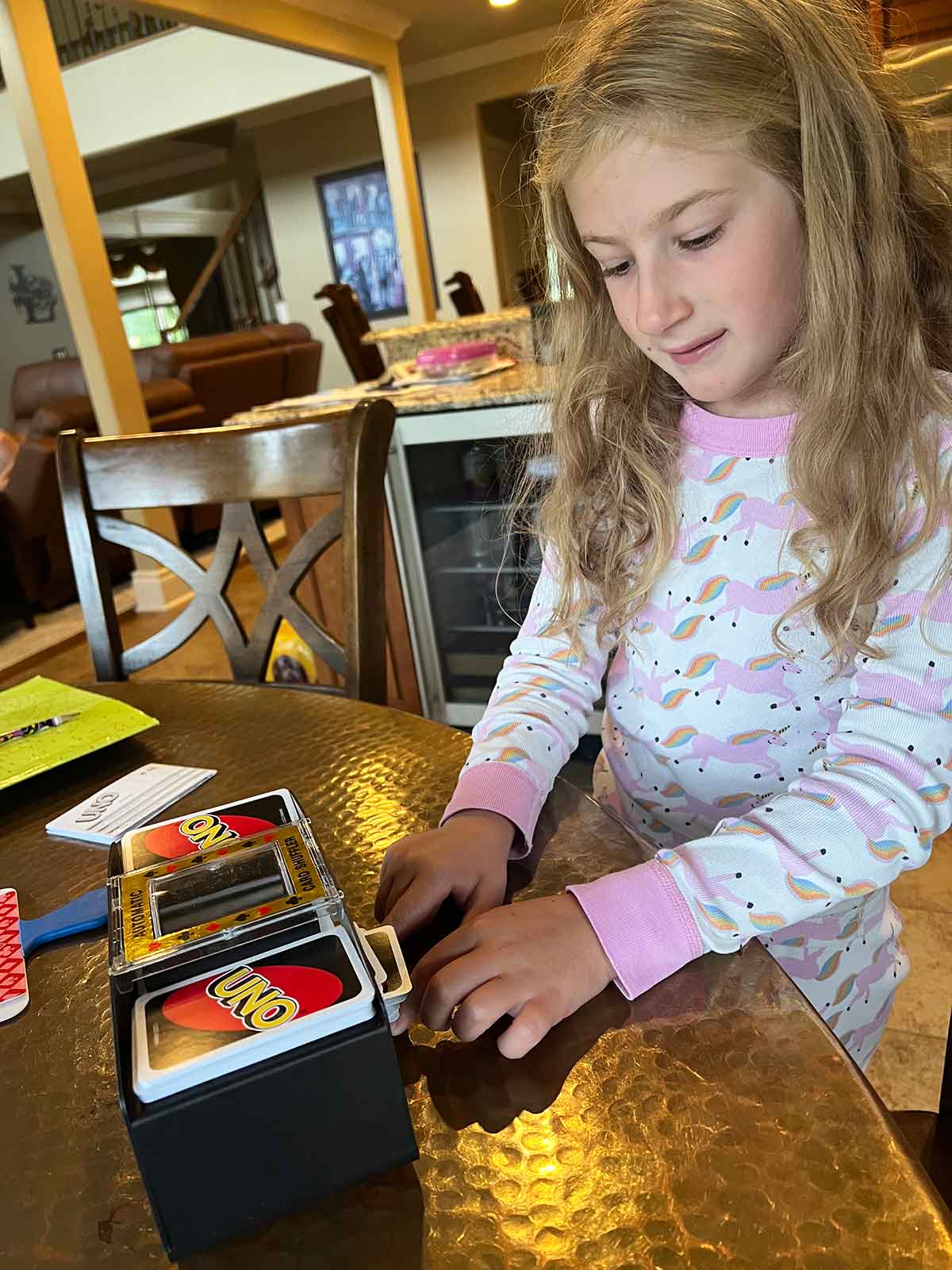 Little girl playing Uno at a kitchen table and using an automatic card shuffler.